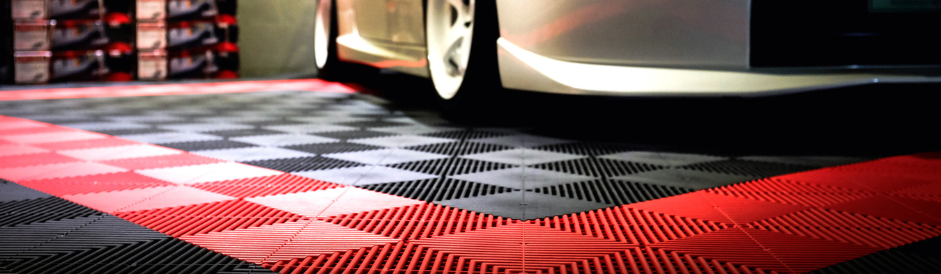 A closeup of Racing Red and Jet Black Swisstrax tiles on a garage floor with a silver car on top