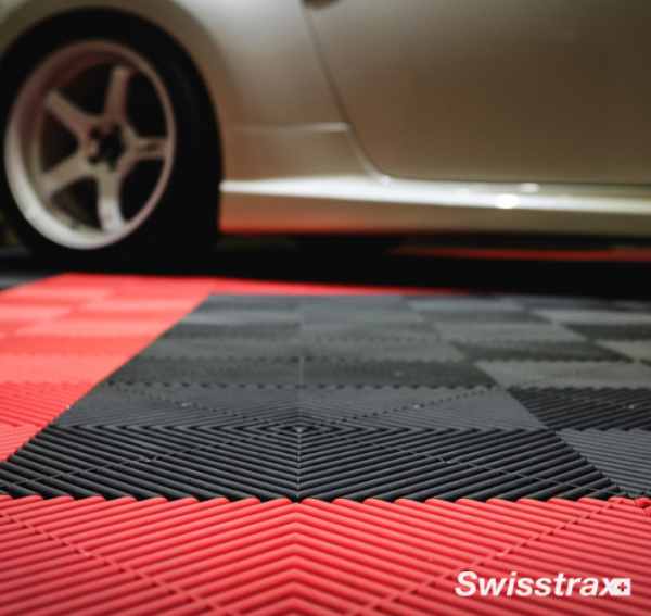 A closeup of a garage with Racing Red and Jet Black Swisstrax tiles as the floor, with a silver car on top