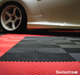 A closeup of a garage with Racing Red and Jet Black Swisstrax tiles as the floor, with a silver car on top