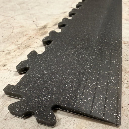 Close up of a Garage Floor Tile Company edge ramp in speckle effect colourway, positioned on a cracked bare concrete floor